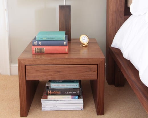 Walnut bedside cabinet with single drawer, stacked books and an alarm clock