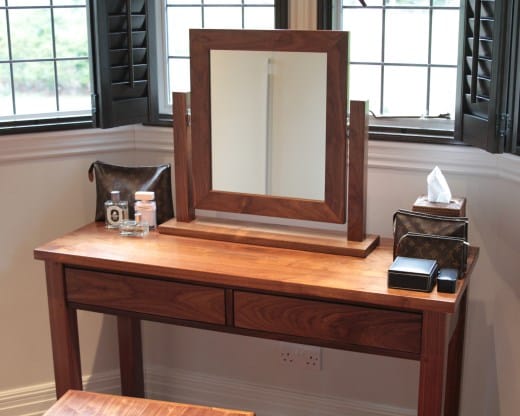 Walnut framed tilting mirror on a matching dressing table by shuttered windows