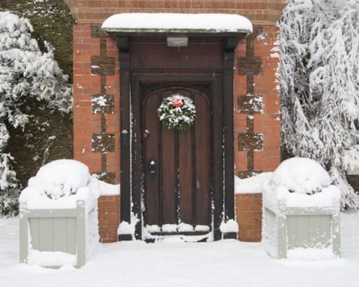Snow-covered grey painted hardwood planters flanking a front door with festive wreath