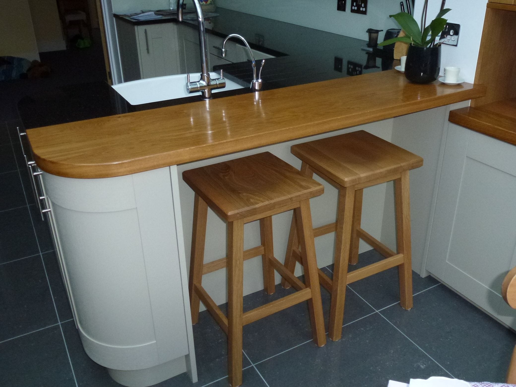 Two oak breakfast-bar stools tucked under a curved oak worktop with matching grain