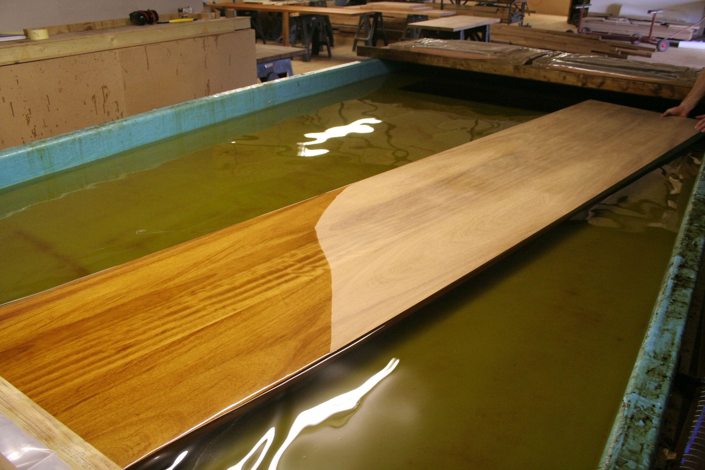 Iroko worktop part-submerged in an oil dip tank, the timber darkening to gold