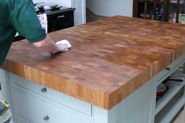 Oiling an end grain oak butcher's block island top in a pale green kitchen