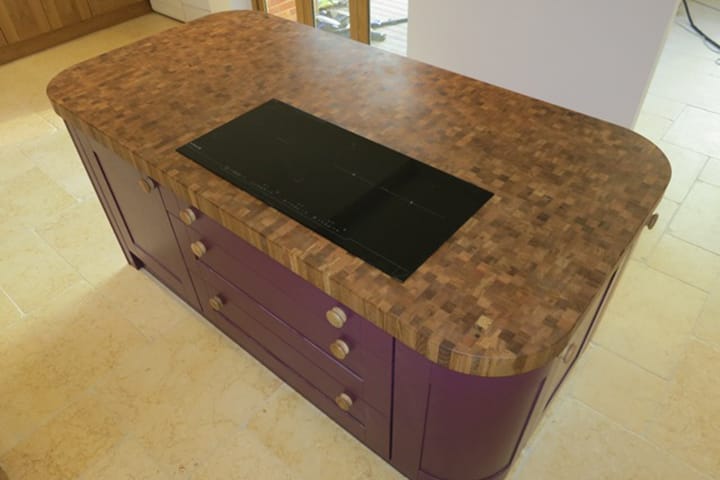 Curved oak end grain worktop with induction hob on a plum-painted kitchen island