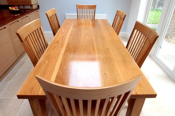 Solid oak dining table with six slat-back oak chairs in a bright kitchen