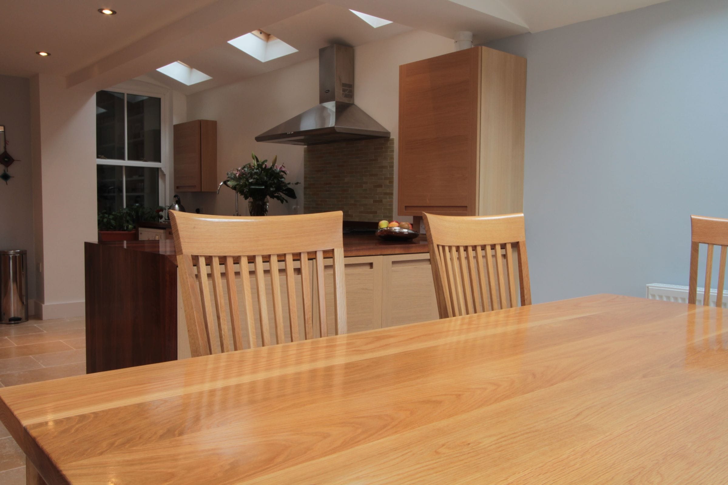 Oak dining table and slat-back chairs in an open-plan kitchen with skylights