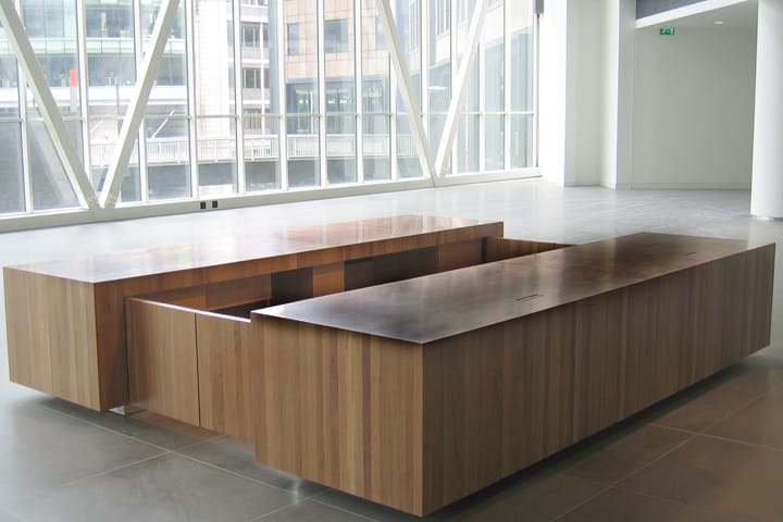 Low rectangular wooden reception furniture in a glazed modern office atrium