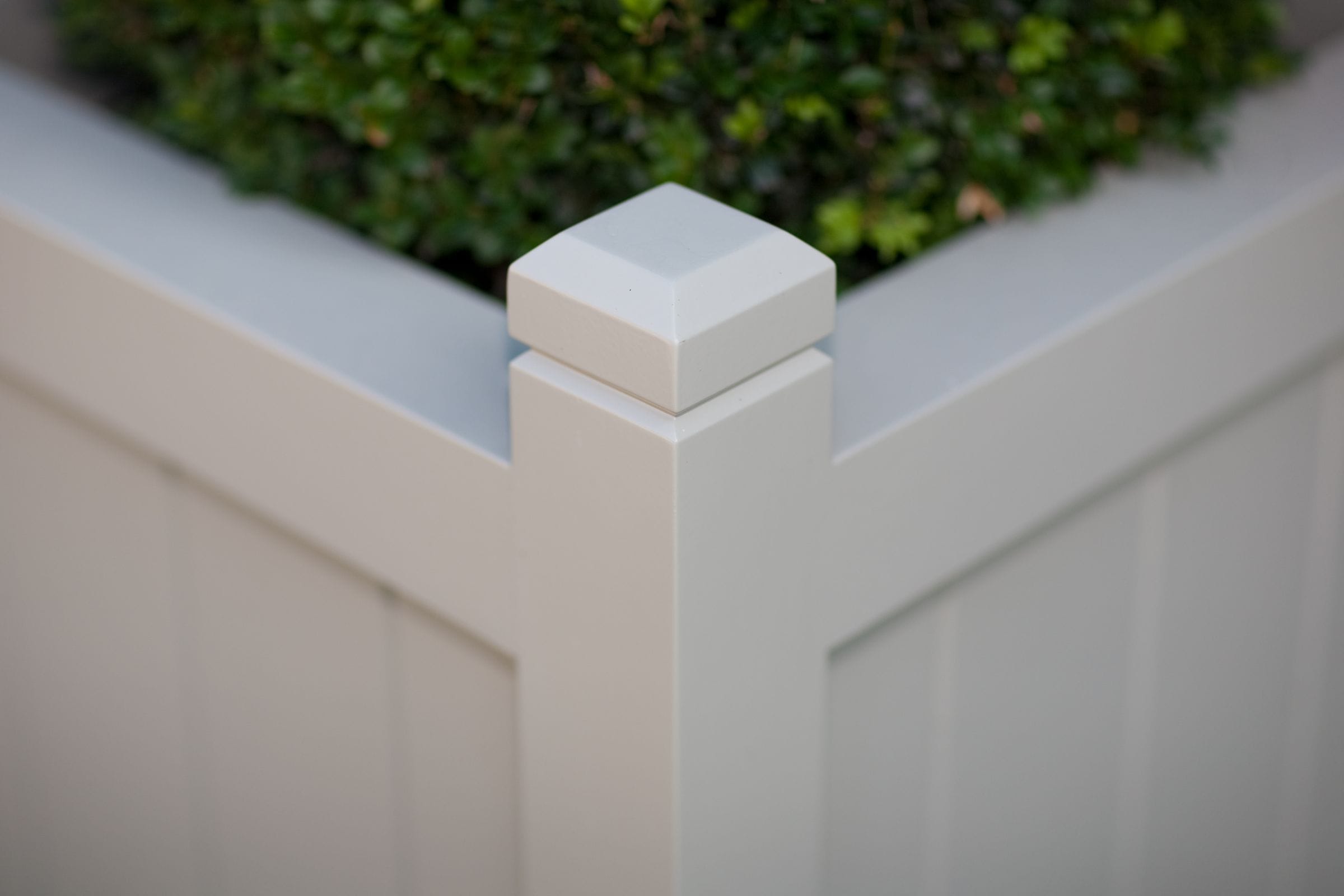 Corner post detail of a grey painted planter with capped finial and box shrub