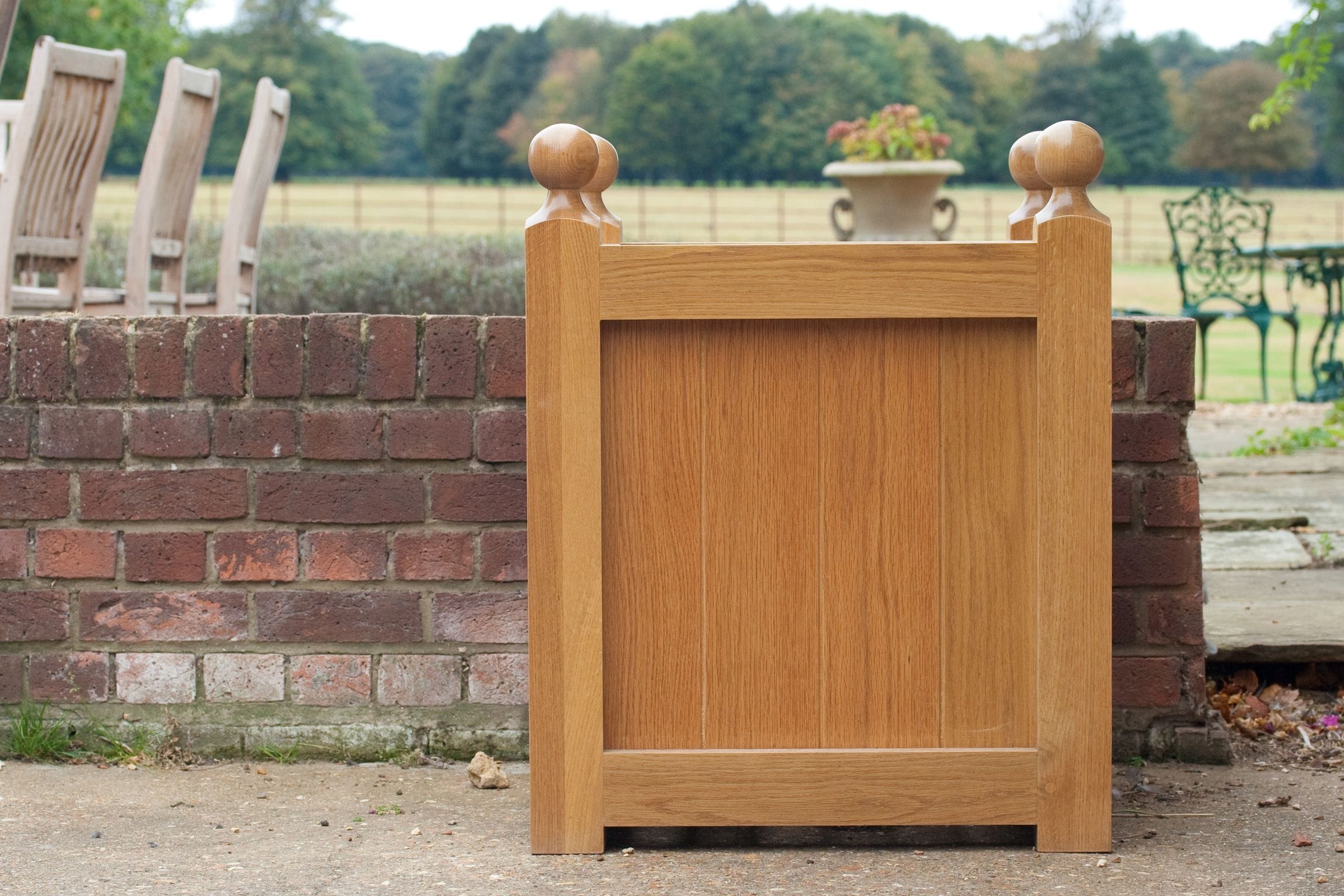 Oak garden planter with ball finials on a patio beside a brick wall