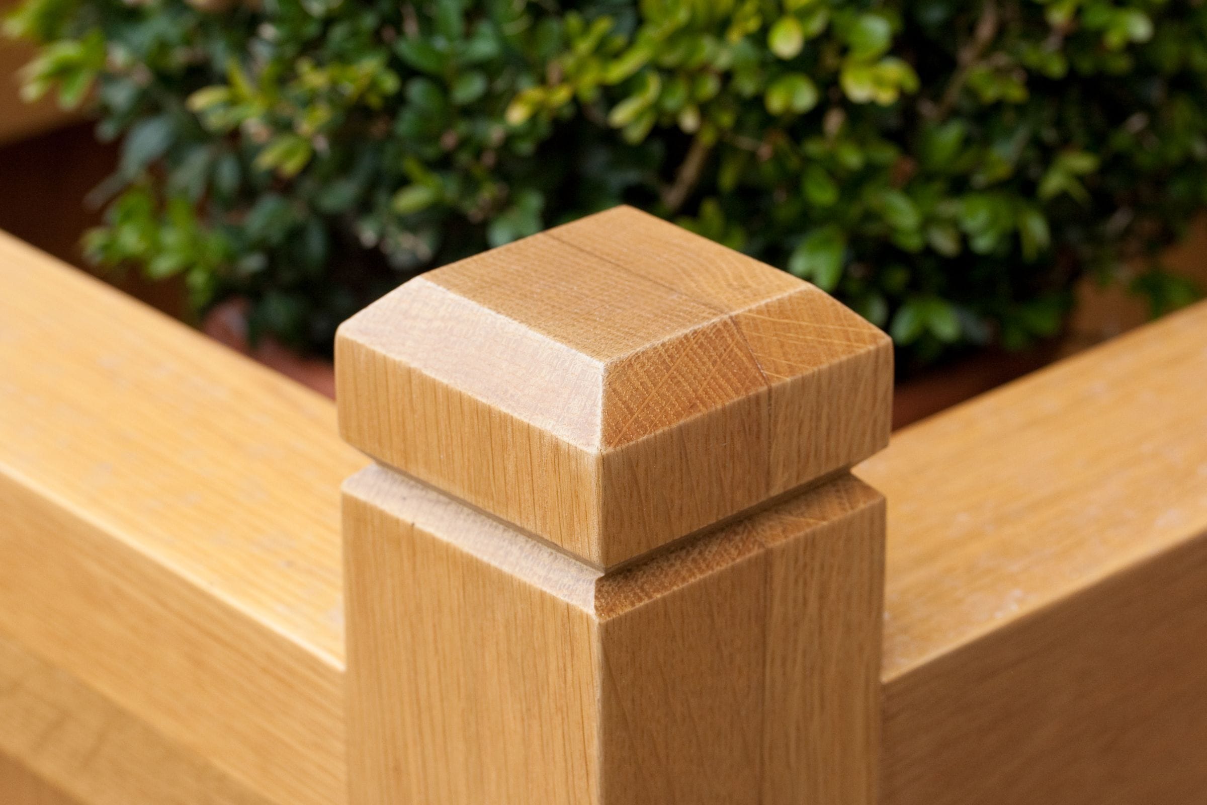 Chamfered square post cap on an oak planter corner, box shrub behind