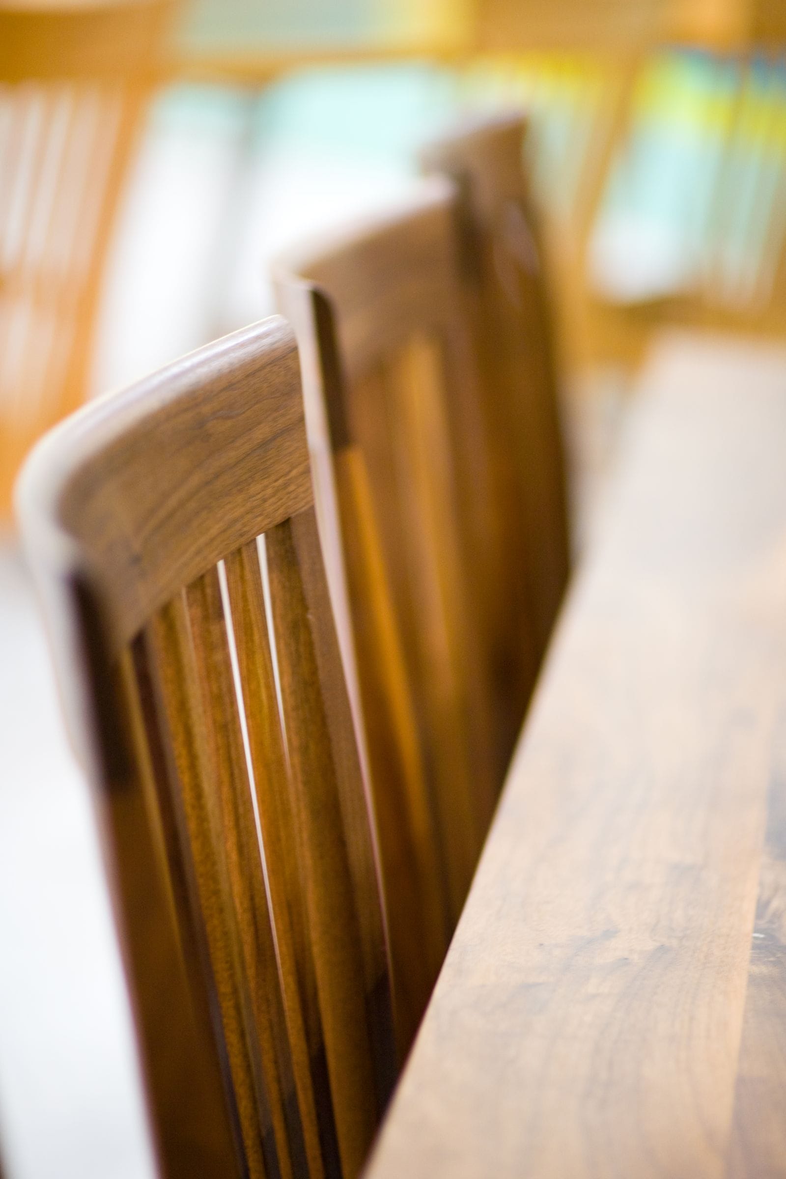 Slatted walnut dining chair backs lined up along a table edge
