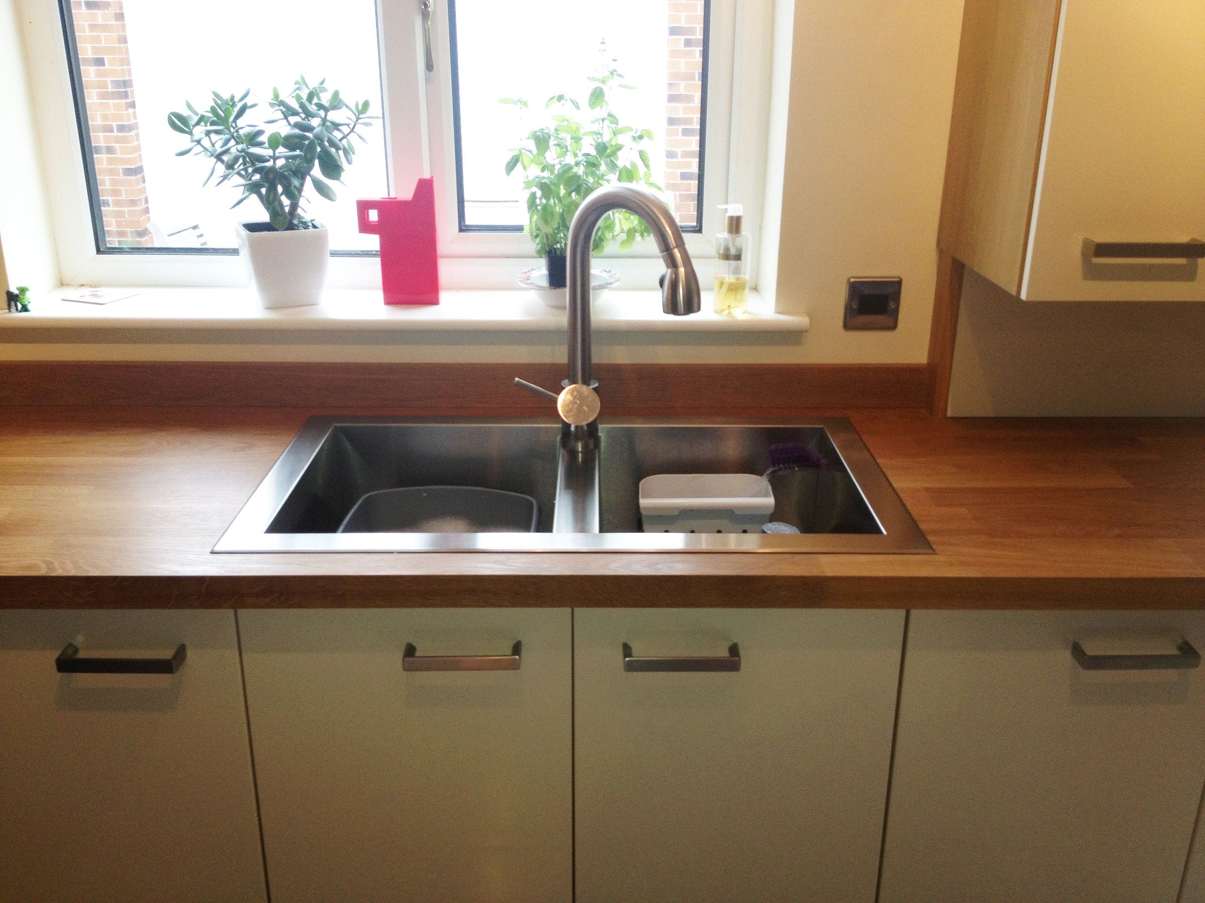 Oak worktop with inset stainless steel sink and swan-neck tap below a kitchen window