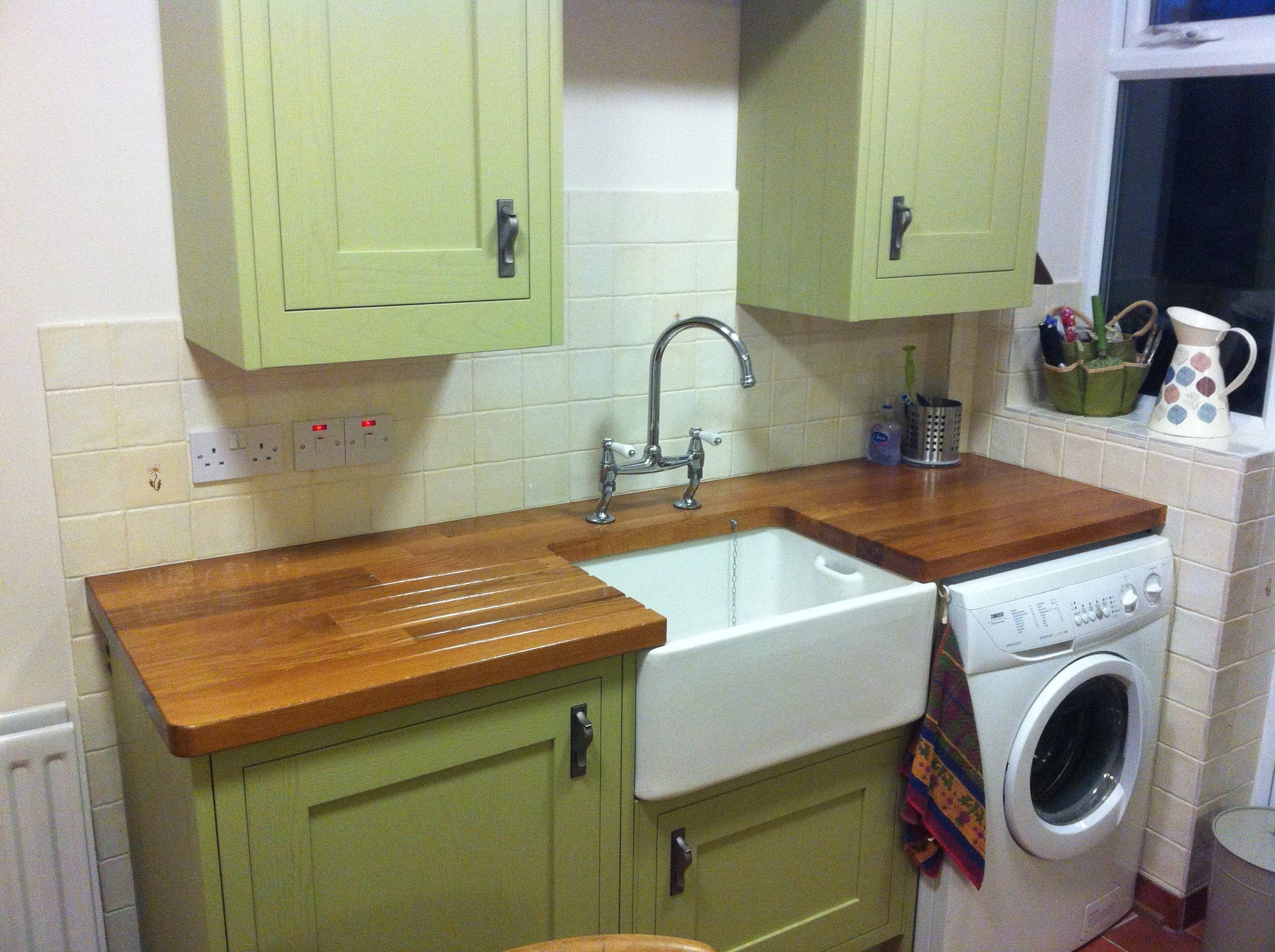 Oak worktop with carved drainer grooves beside a Belfast sink and green cabinets