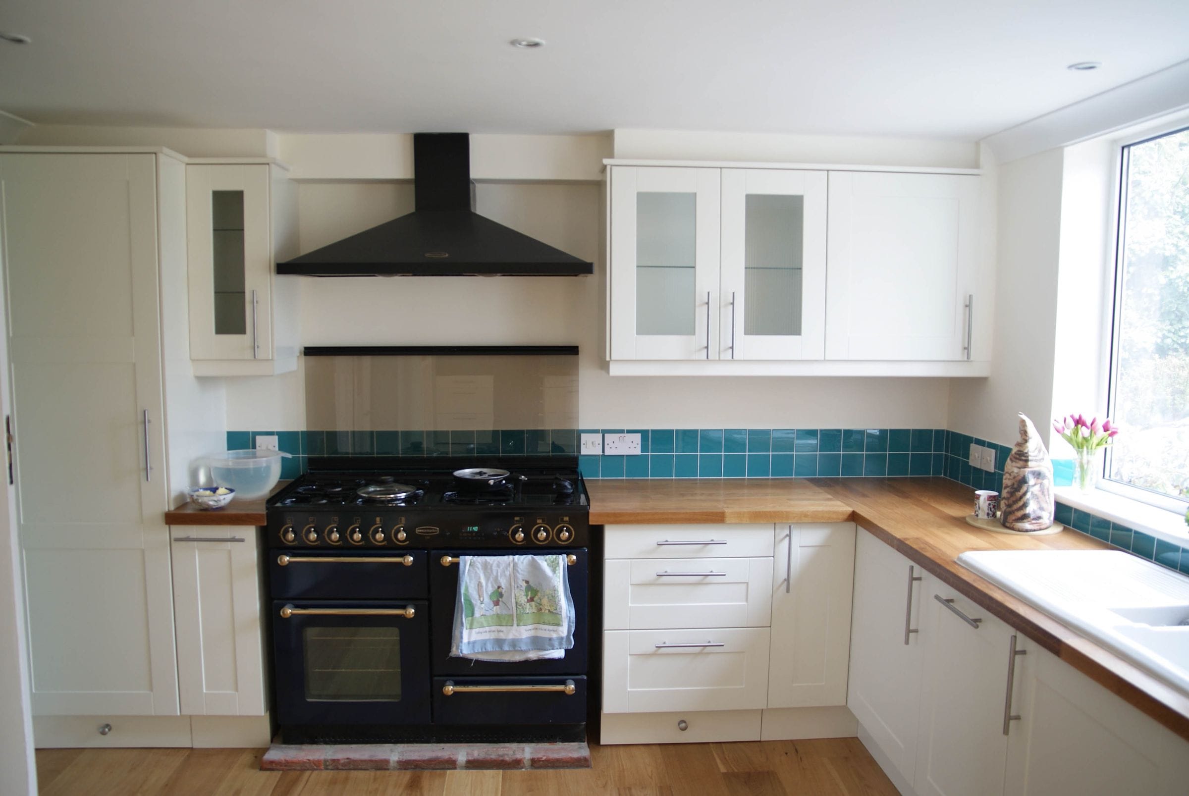 Cream kitchen with black range cooker, teal tiled splashback and oak worktops