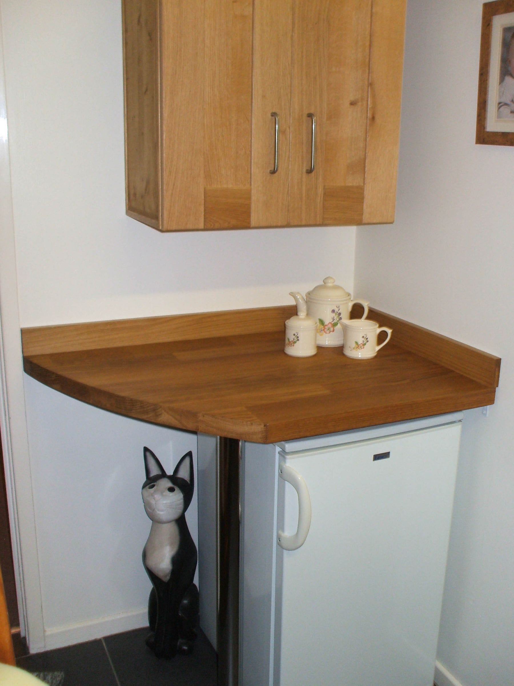 Curved oak counter over an under-counter fridge with a china tea set