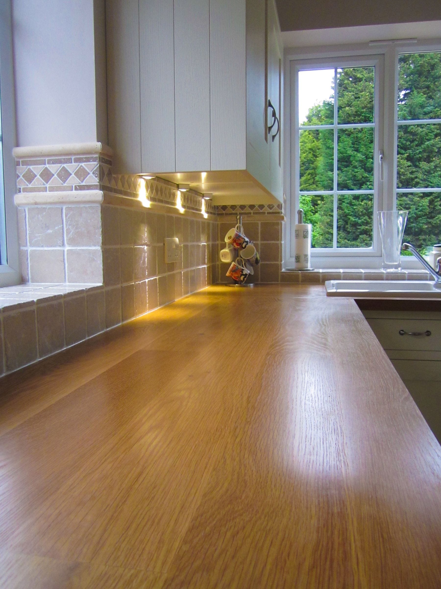 Long oak worktop under cabinet lighting with stone tiled splashback
