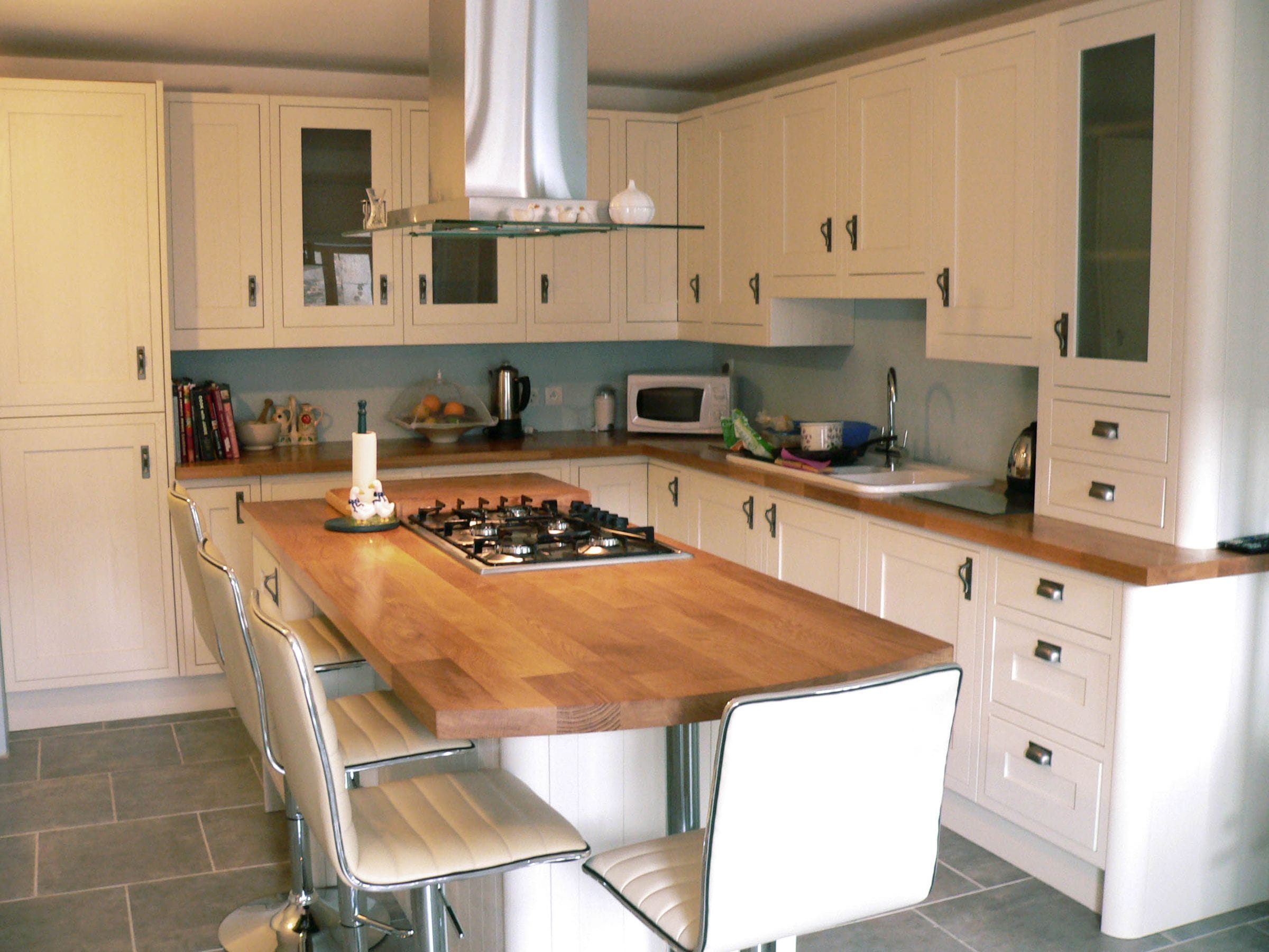 Oak-topped kitchen island with inset gas hob and white leather bar stools