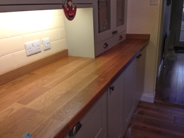 Oak worktop on grey painted units lit by under-cabinet lighting