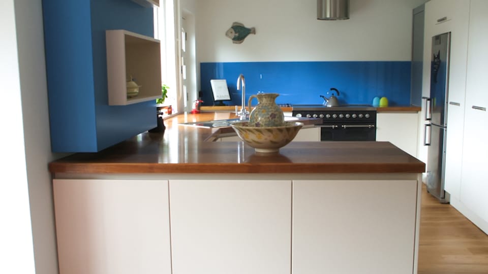 Dark oiled oak worktop on a white handleless peninsula with blue splashback