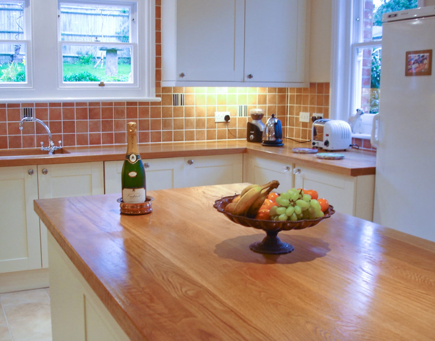 Oak island worktop with fruit stand and champagne, terracotta tiled walls behind