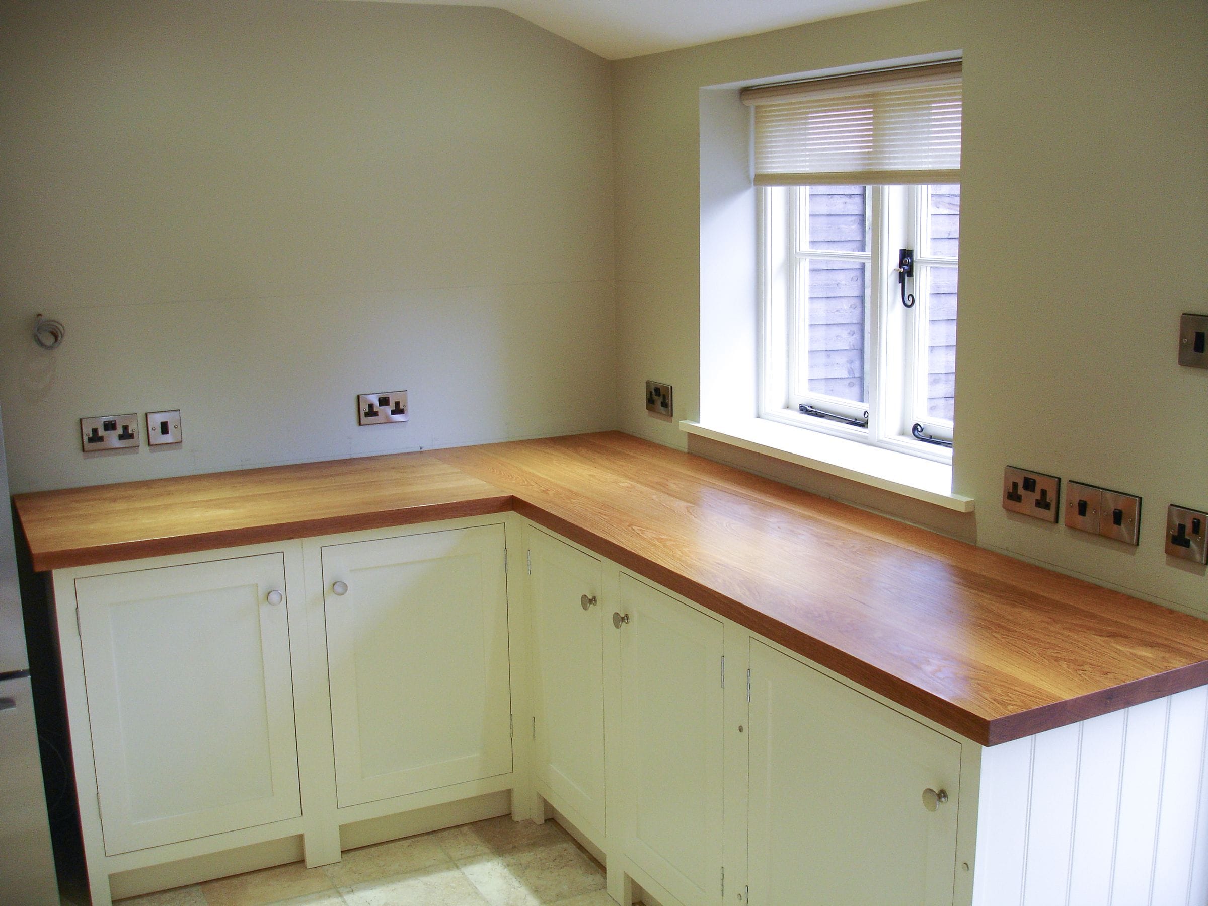 Newly fitted oak super stave worktop on cream in-frame units by a window