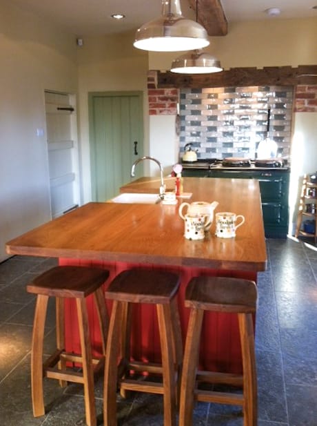 Oak-topped island with red base, wooden stools and green range cooker behind