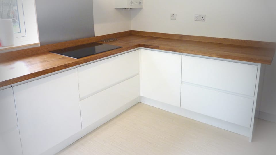 L-shaped oak worktop with inset black hob in a white handleless kitchen