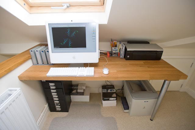 Oak desk top under a loft skylight holding a computer, keyboard and printer