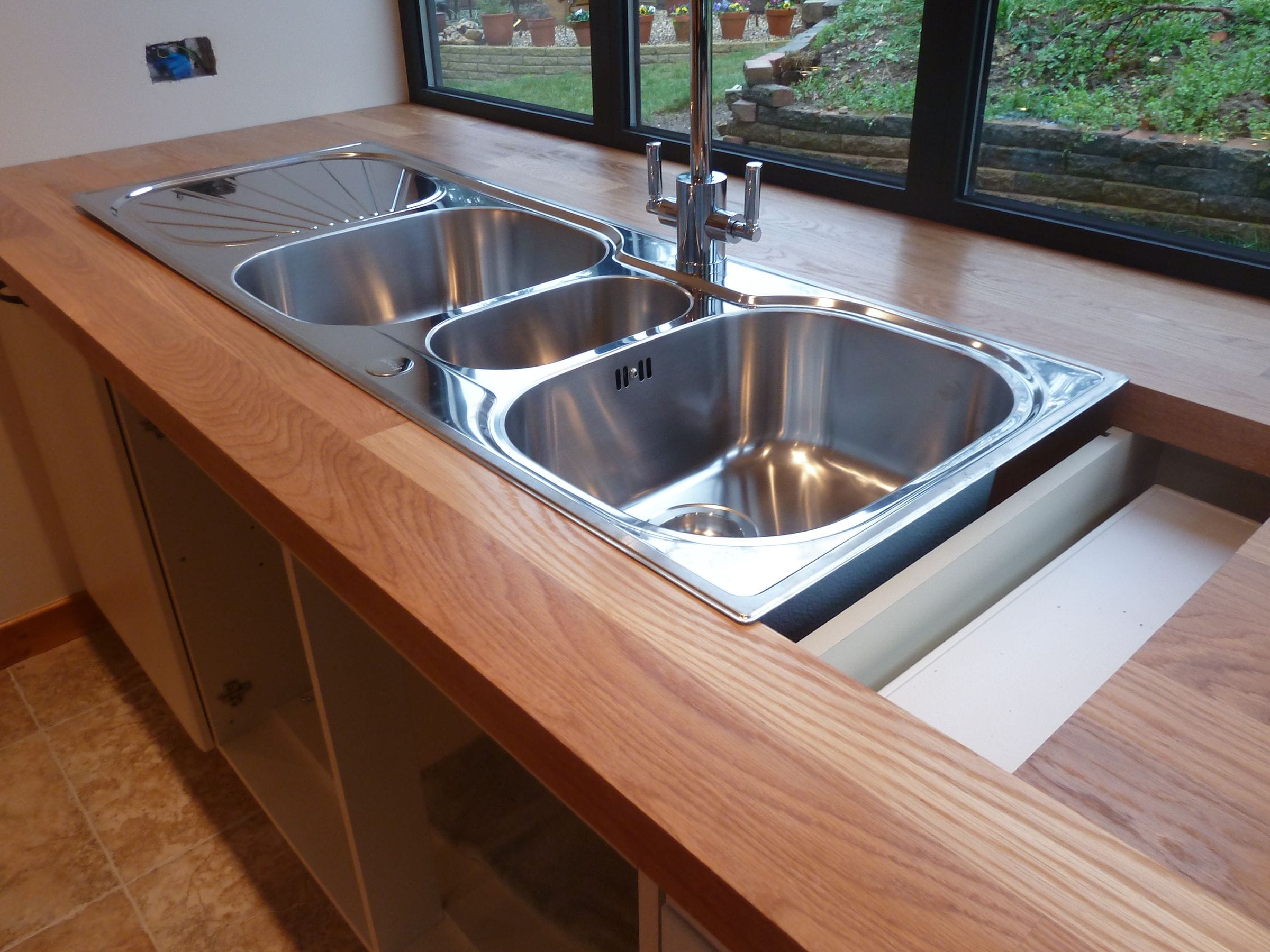 Stainless steel double sink and drainer set into an oak worktop below garden windows