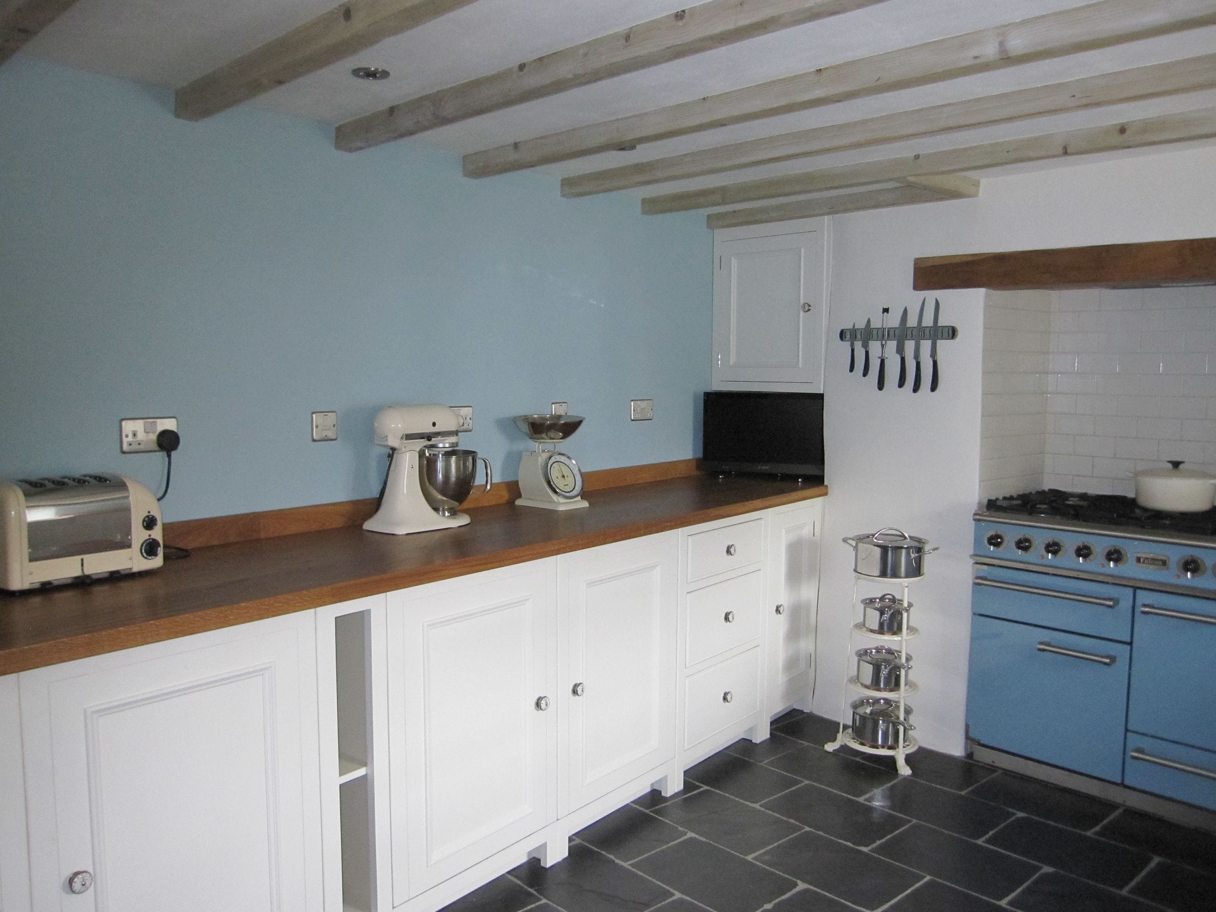 Beamed kitchen with oak worktop, white cabinets, blue range cooker and slate floor