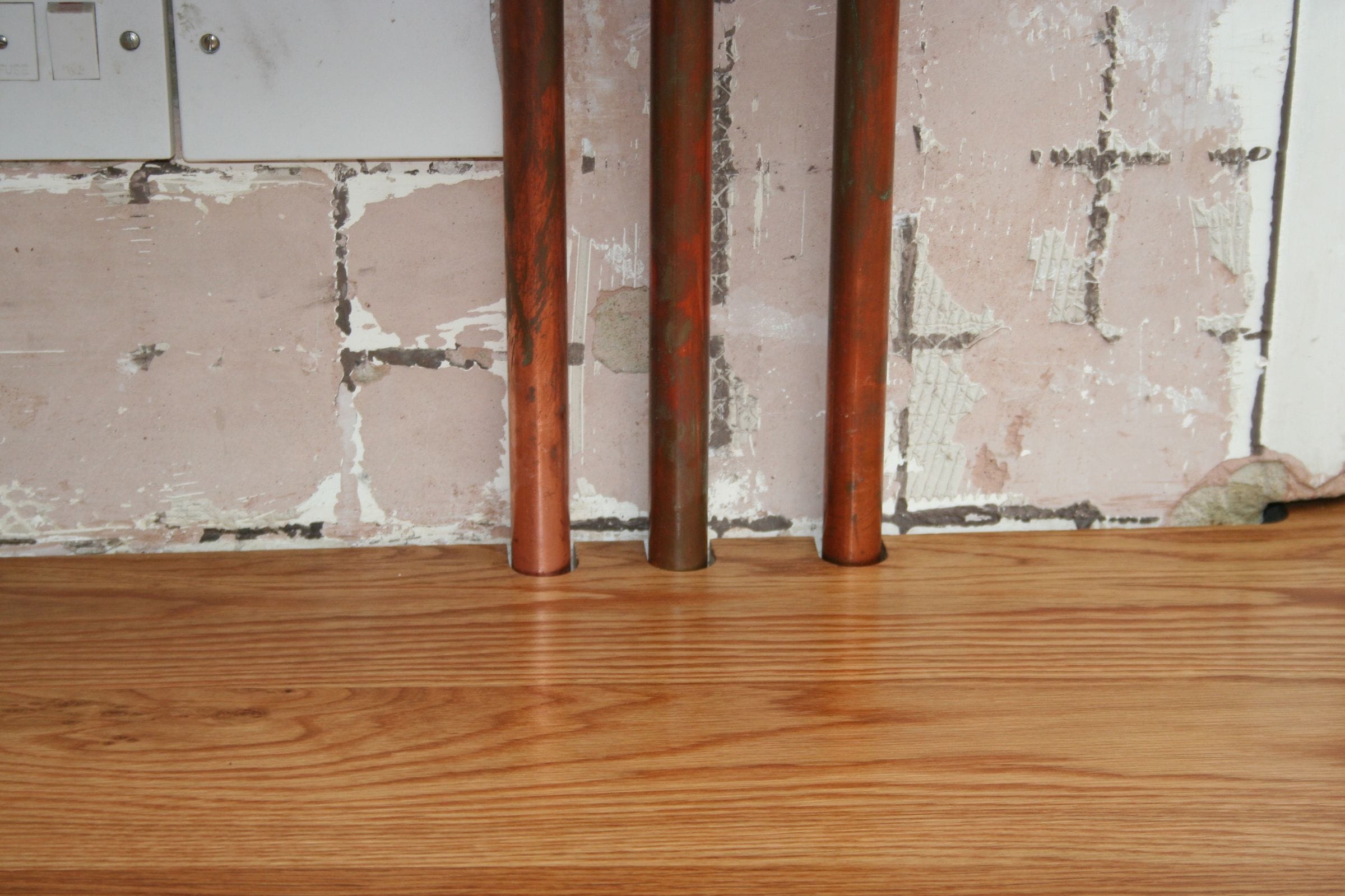 Copper pipes passing through neat cutouts in an oak worktop against a bare wall