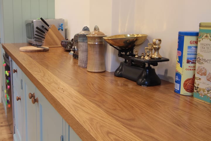 Oiled oak worktop on pale blue cabinets with vintage brass balance scales and tins