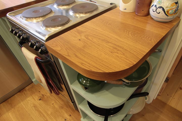 Curved oak worktop with rounded corner beside an electric cooker and green shelving