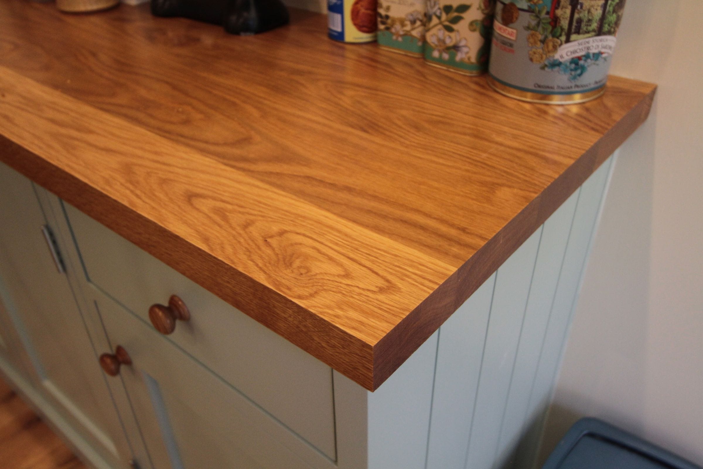 Corner detail of a thick oak worktop with swirling grain on sage green cabinets