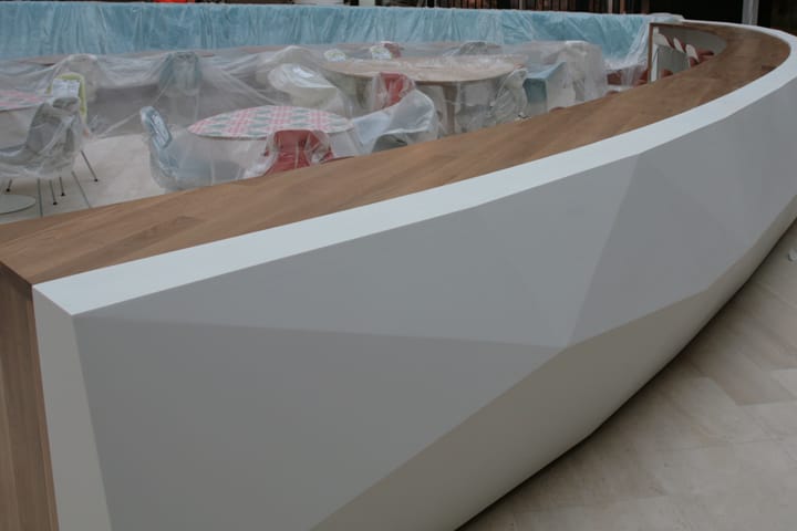 Long curved wooden counter top on a faceted white bar in a cafe seating area