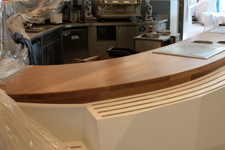 Curved wooden bar top being fitted in a commercial kitchen during installation