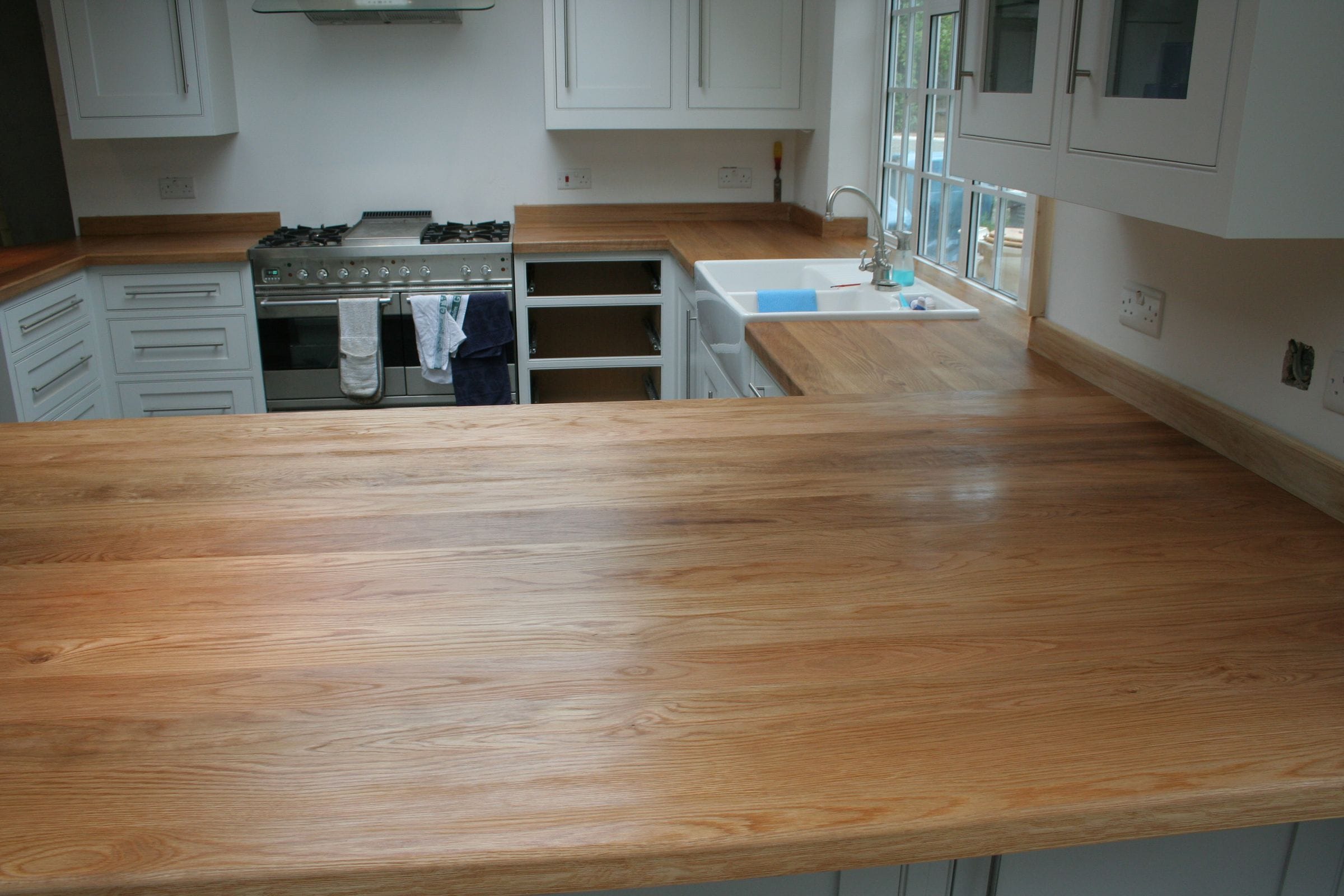 Wide oak peninsula worktop in a white kitchen with range cooker and Belfast sink