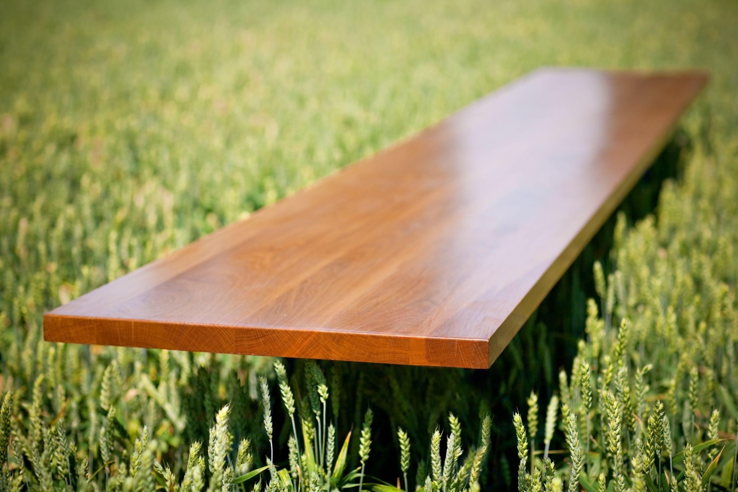 Full-length oiled oak worktop laid across a green wheat field in sunshine