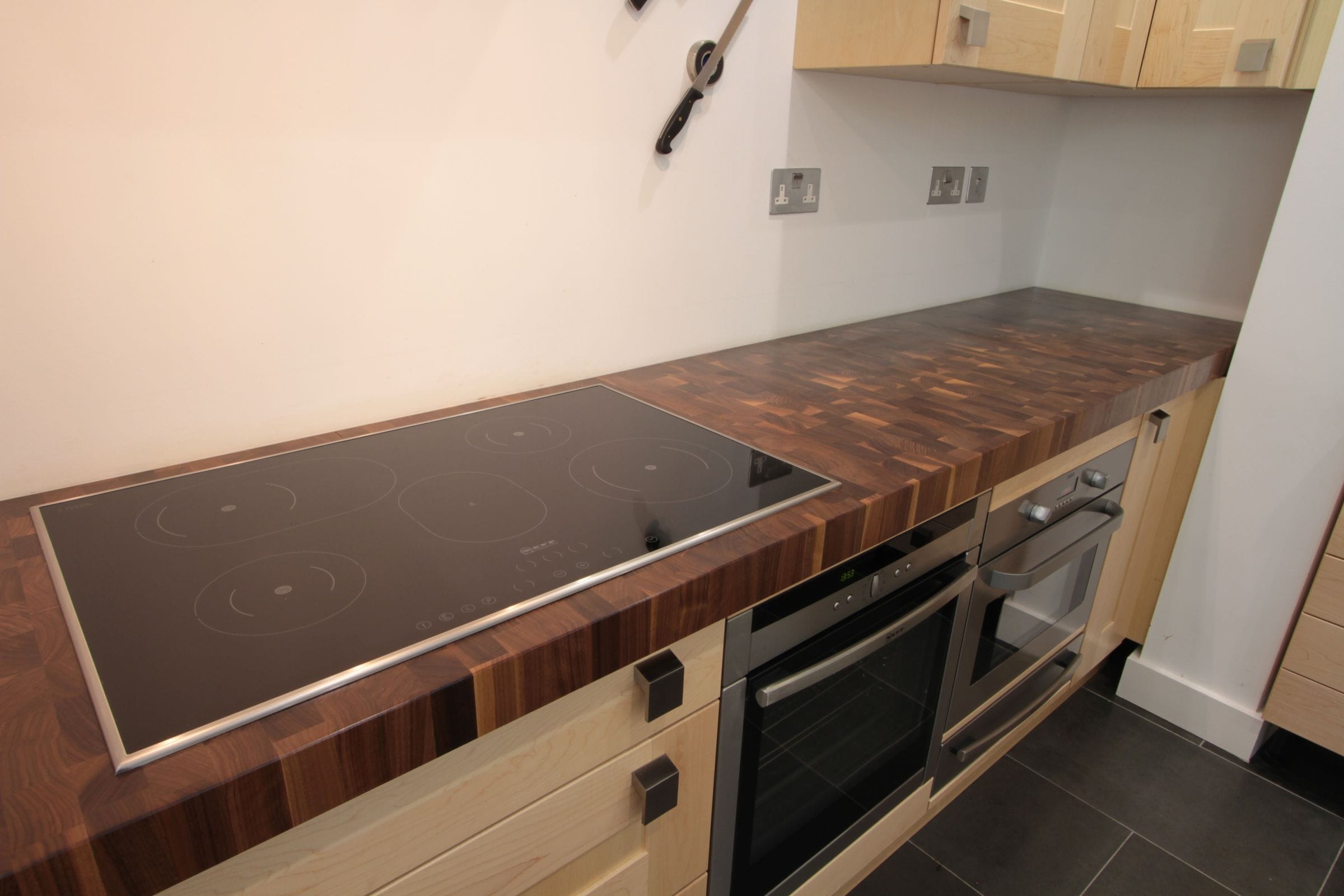 Walnut end grain worktop with inset induction hob above stainless steel ovens