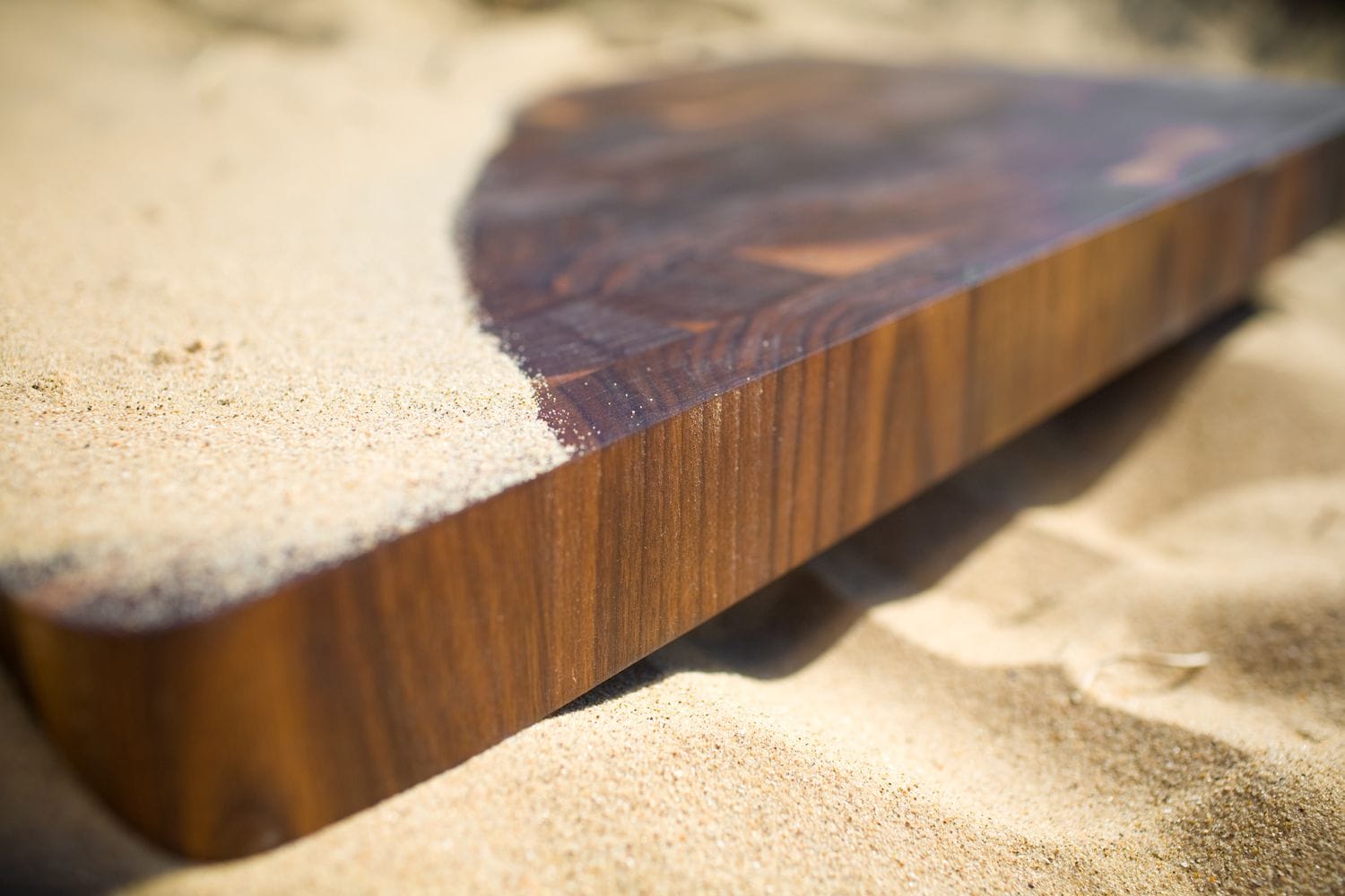 Walnut end grain chopping board resting on sand, edge grain in close-up
