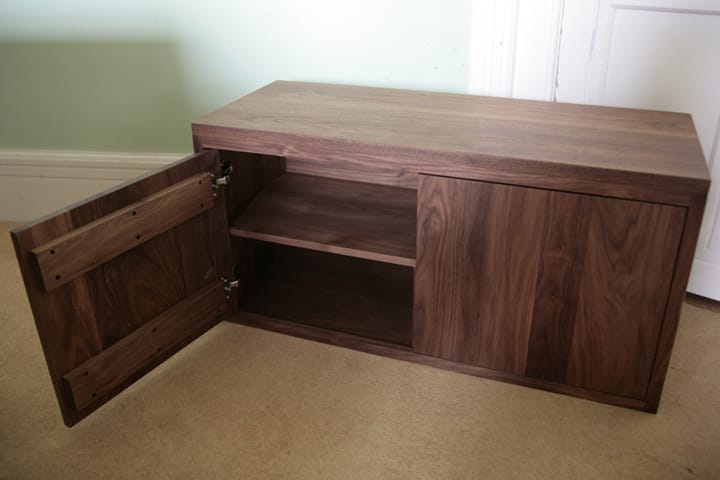 Low walnut media cabinet with one door open showing an internal shelf