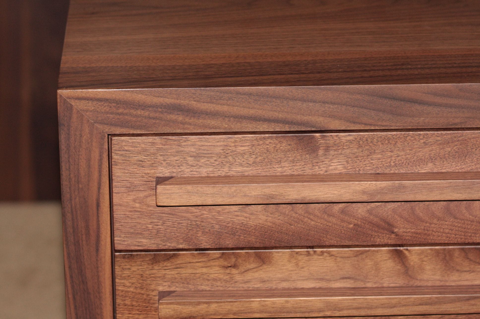 Corner detail of a walnut chest showing mitred frame and slim bar drawer handles