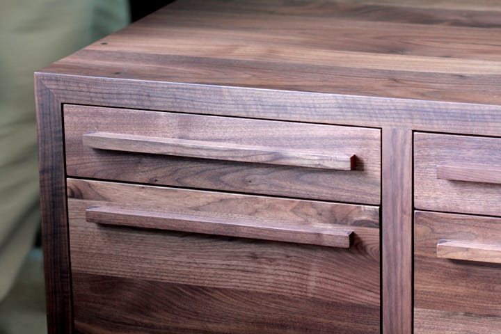 Close-up of slender walnut bar handles on a chest of drawers