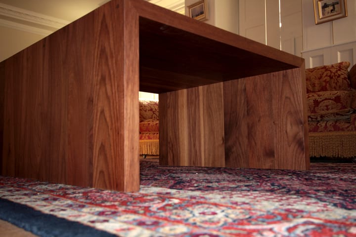 Low walnut waterfall coffee table on a patterned rug in a sitting room