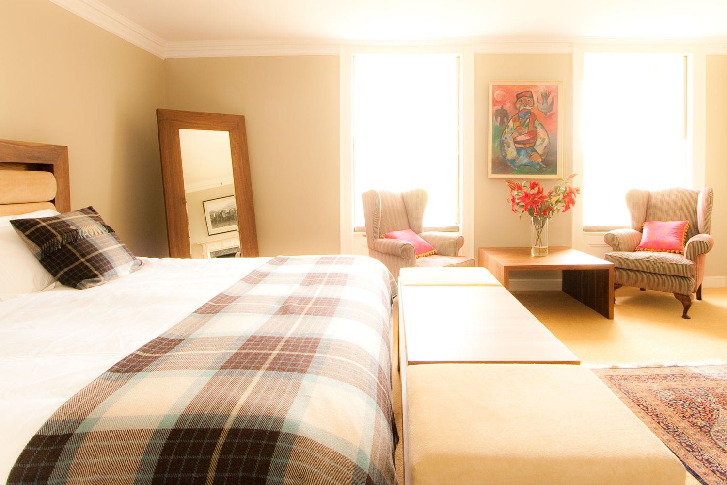Sunlit bedroom with walnut coffee table, bench and mirror beside armchairs