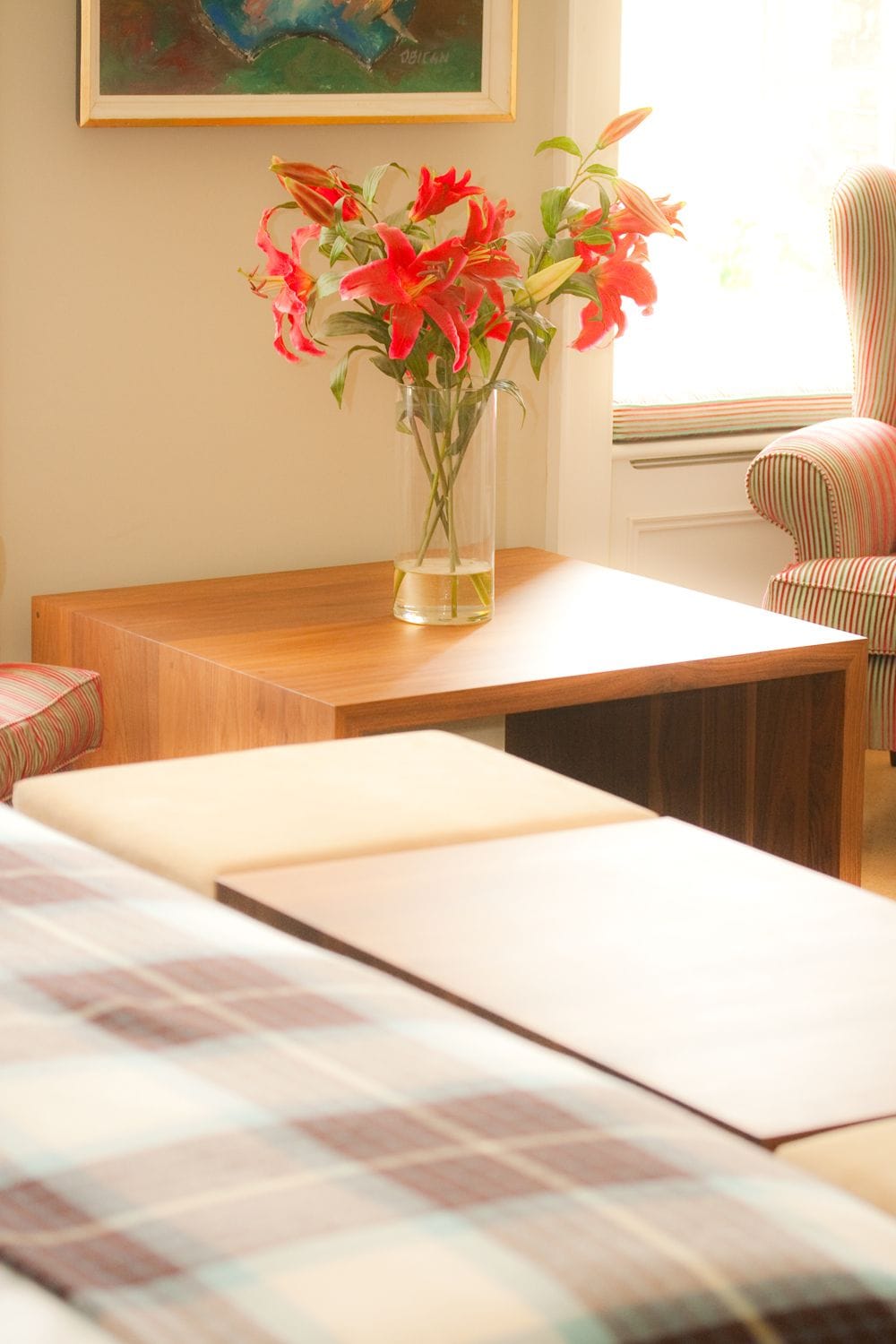 Vase of red lilies on a walnut side table beside an upholstered bench