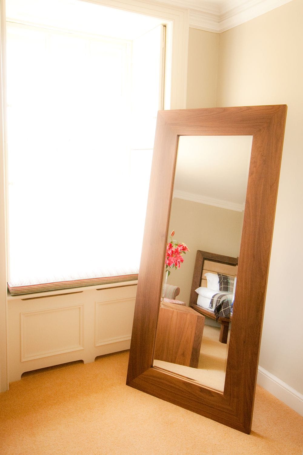 Full-length walnut-framed mirror leaning against a bedroom wall