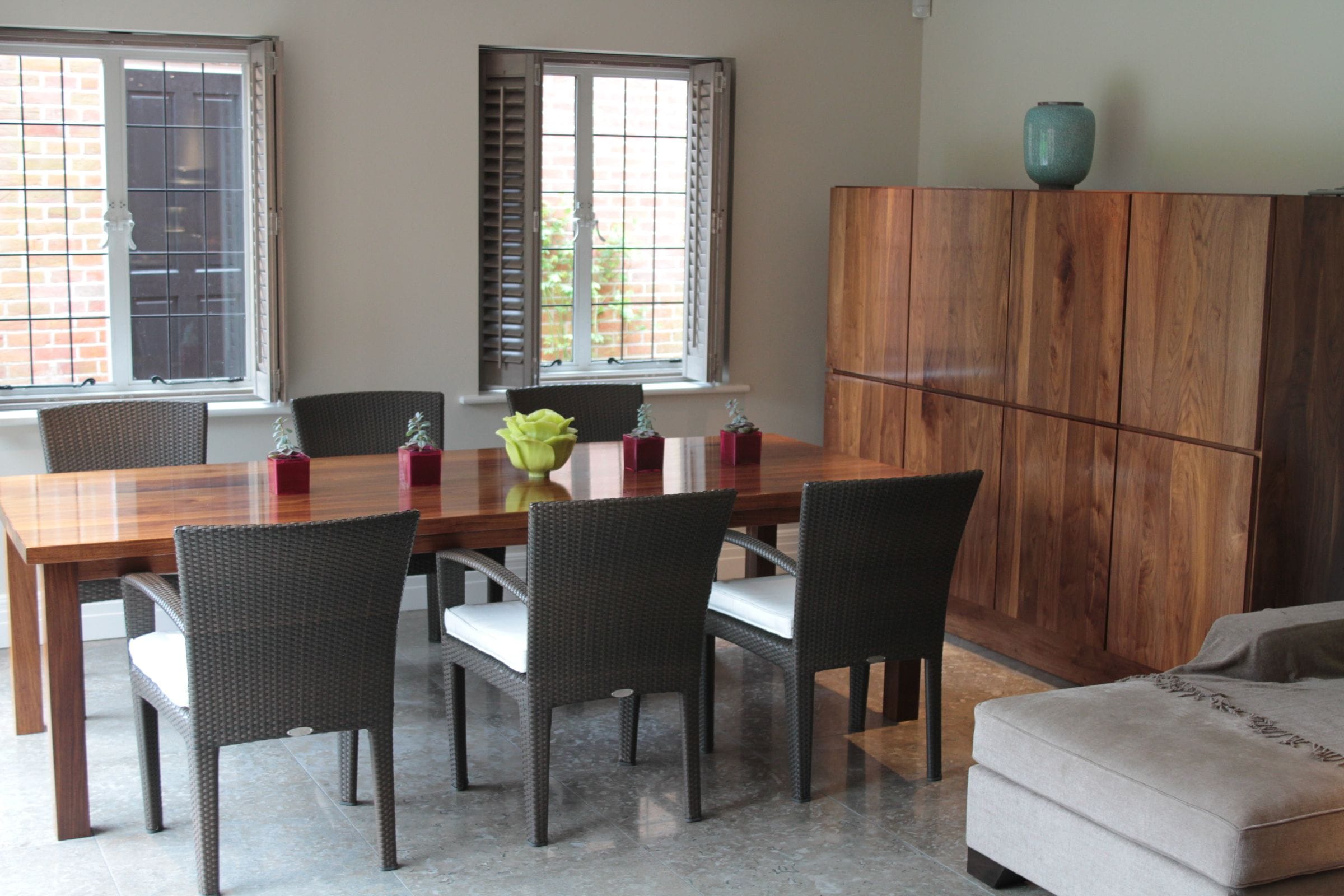 Walnut dining table and tall cupboard in a dining room with rattan chairs