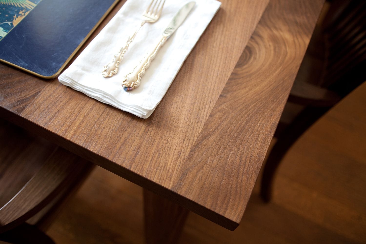 Corner of a walnut dining table with vintage cutlery on a folded linen napkin