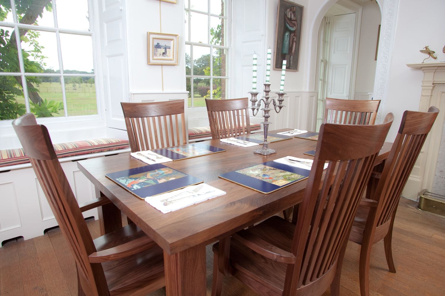 Walnut dining table laid with placemats and candelabra, surrounded by six slatted chairs