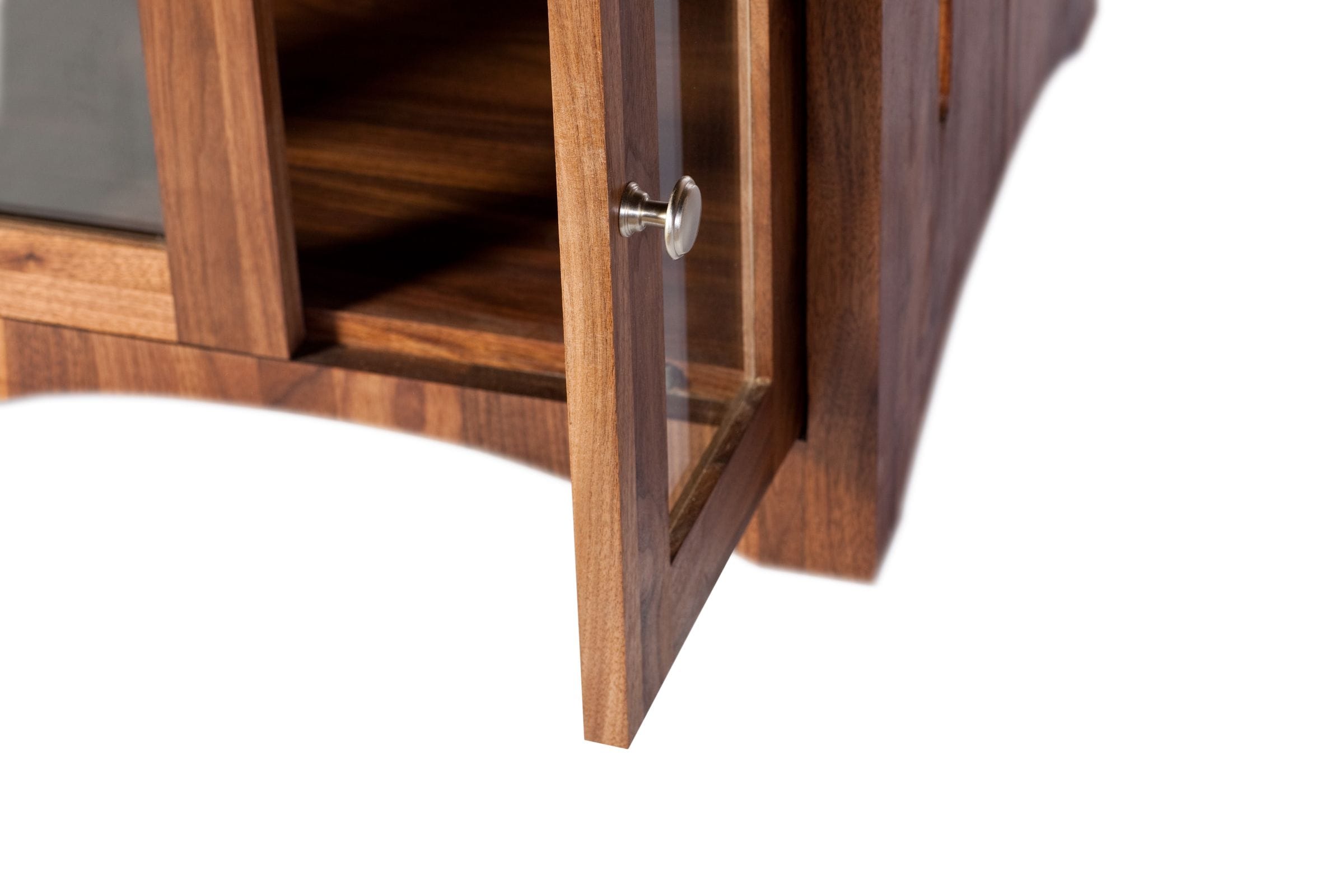 Detail of an open glazed walnut cabinet door with brushed-steel knob